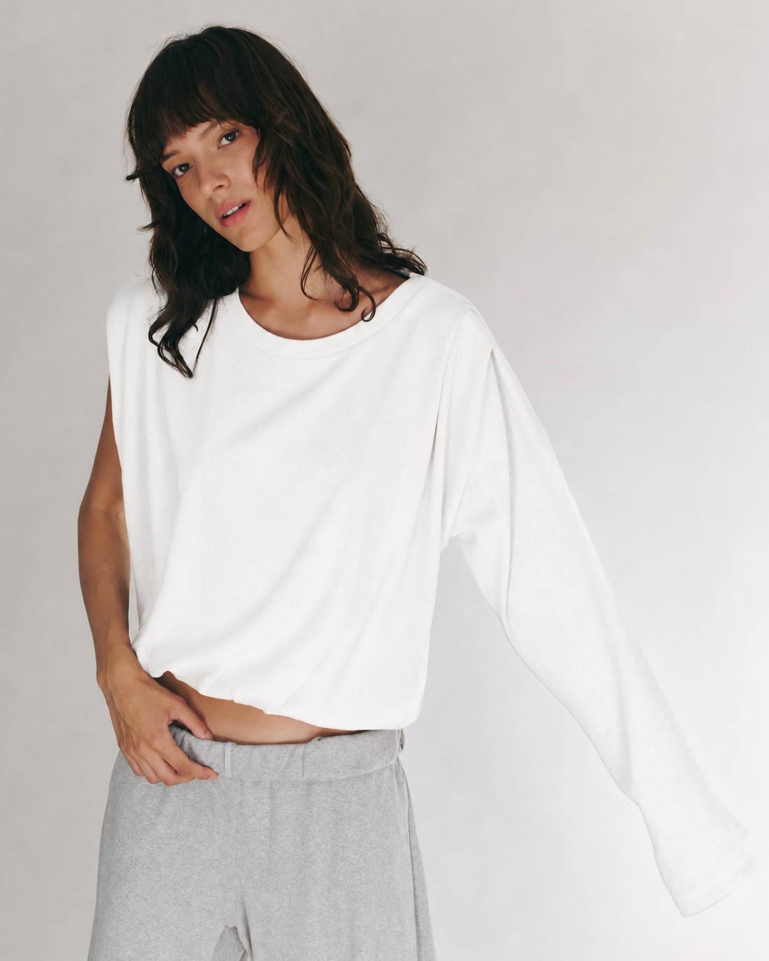 A model wearing a white long-sleeve crop top and light gray sweatpants, photographed against a plain light gray studio background.