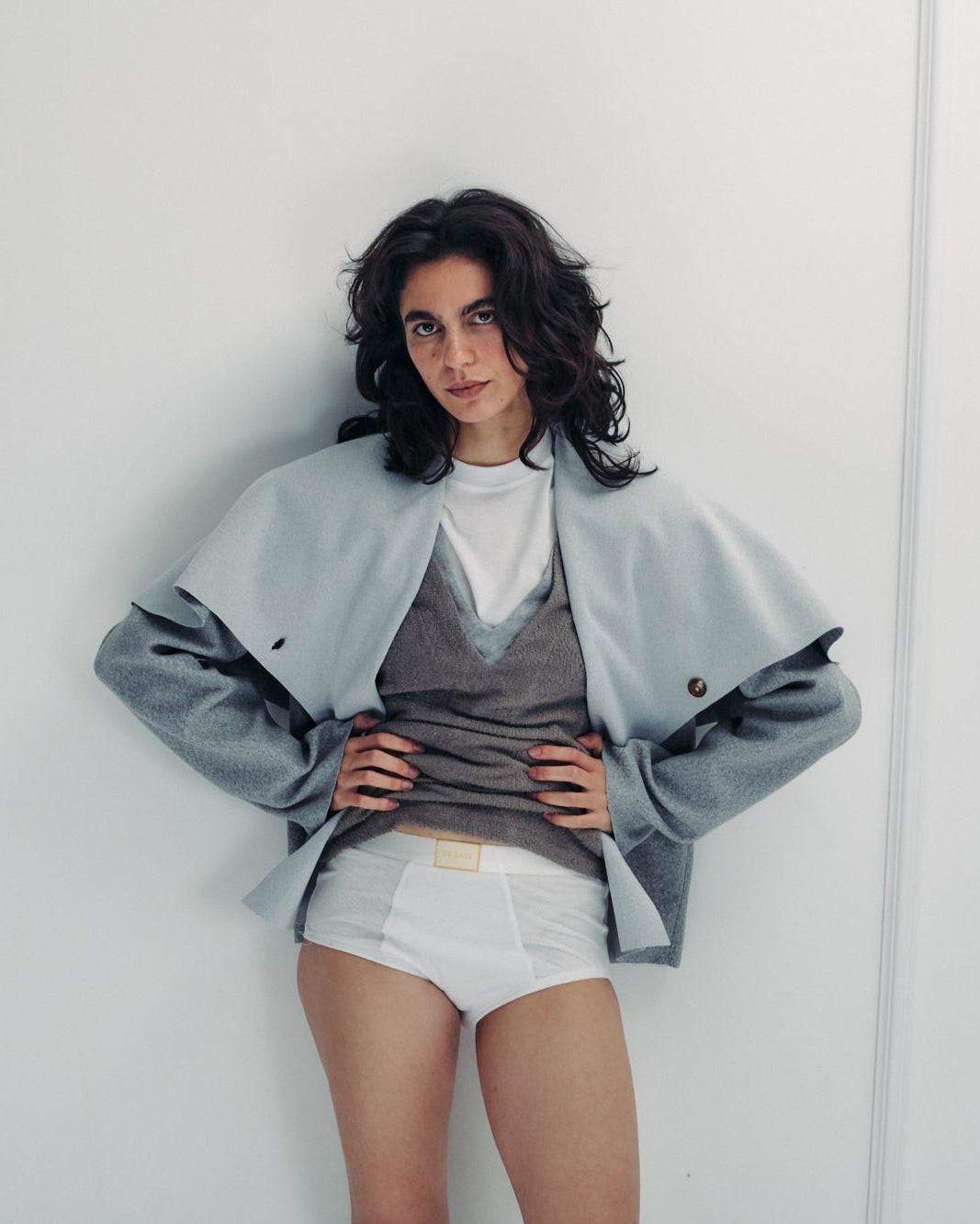 Woman wearing a light gray jacket over a white shirt and shorts against a white background
